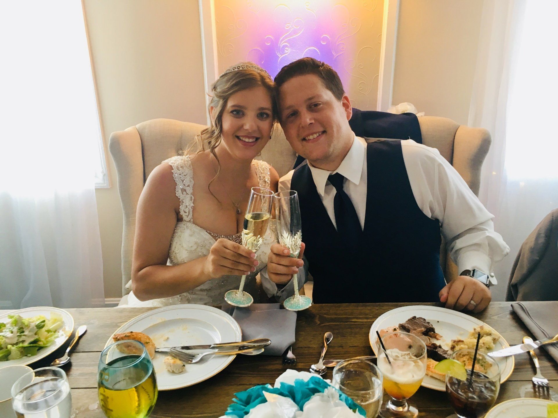 A bride and groom are sitting at a table holding champagne glasses.