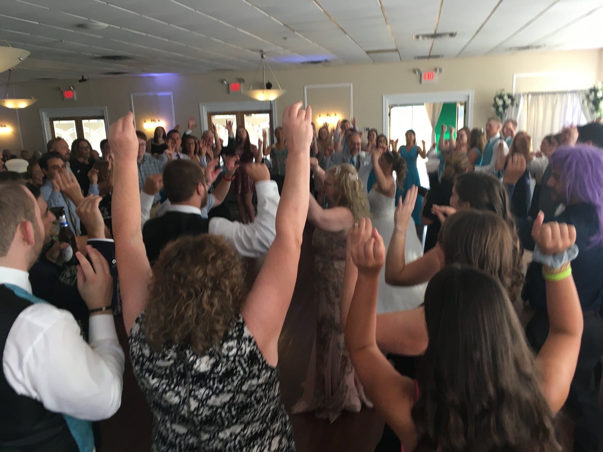 A large group of people are dancing in a room with their arms in the air.