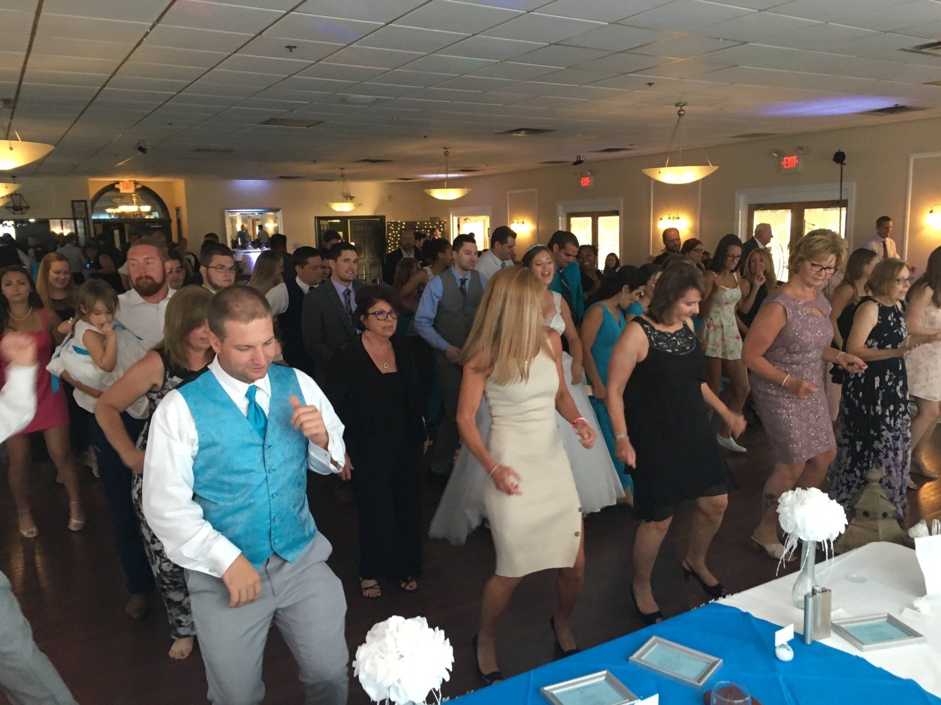 A large group of people are dancing at a wedding reception.