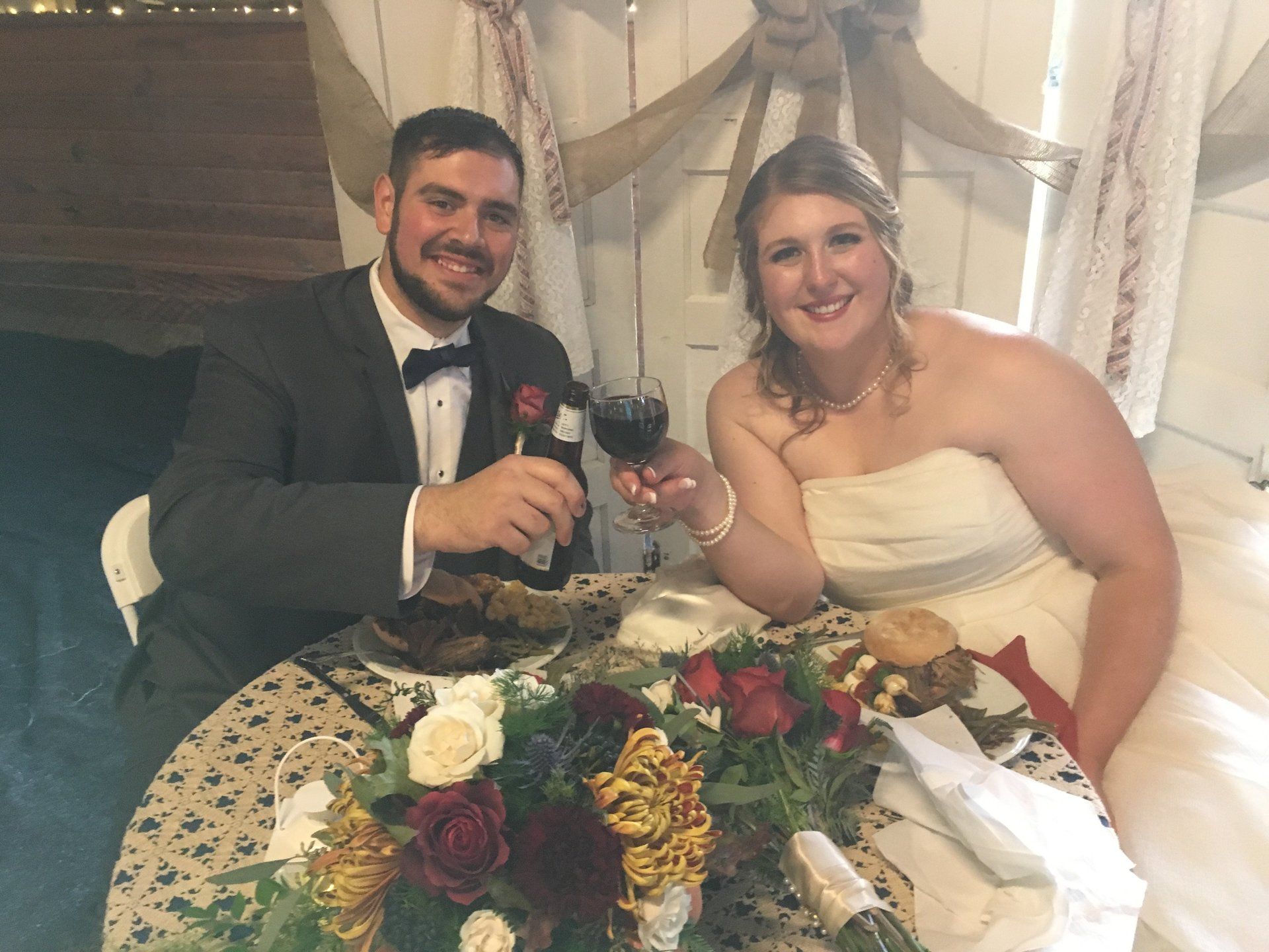 A bride and groom are sitting at a table toasting with wine glasses.