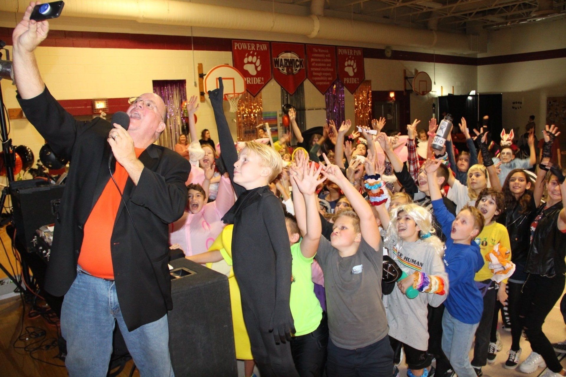 A man is taking a selfie with a microphone in front of a crowd of people.