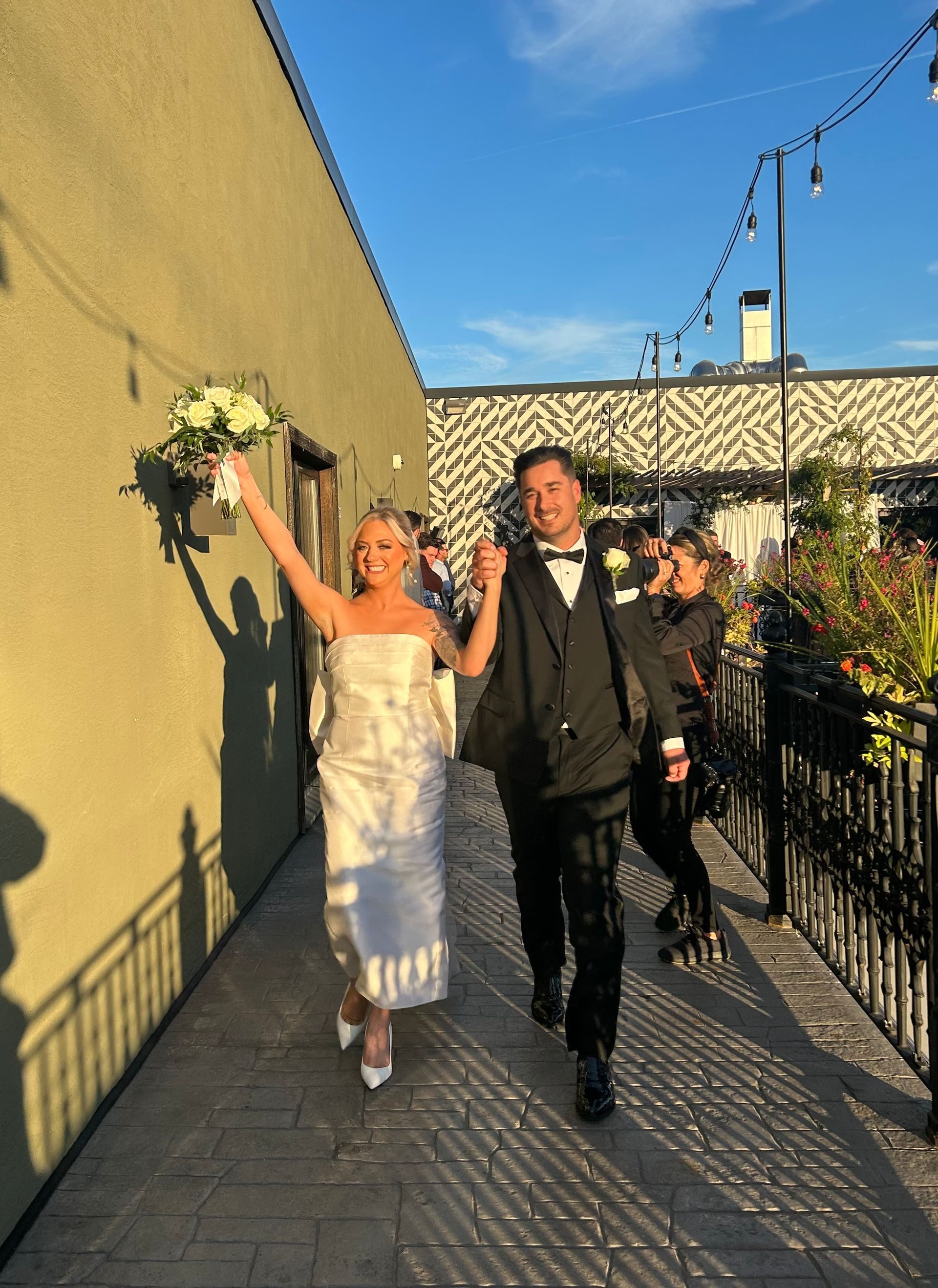 A bride and groom are walking down a sidewalk holding hands.