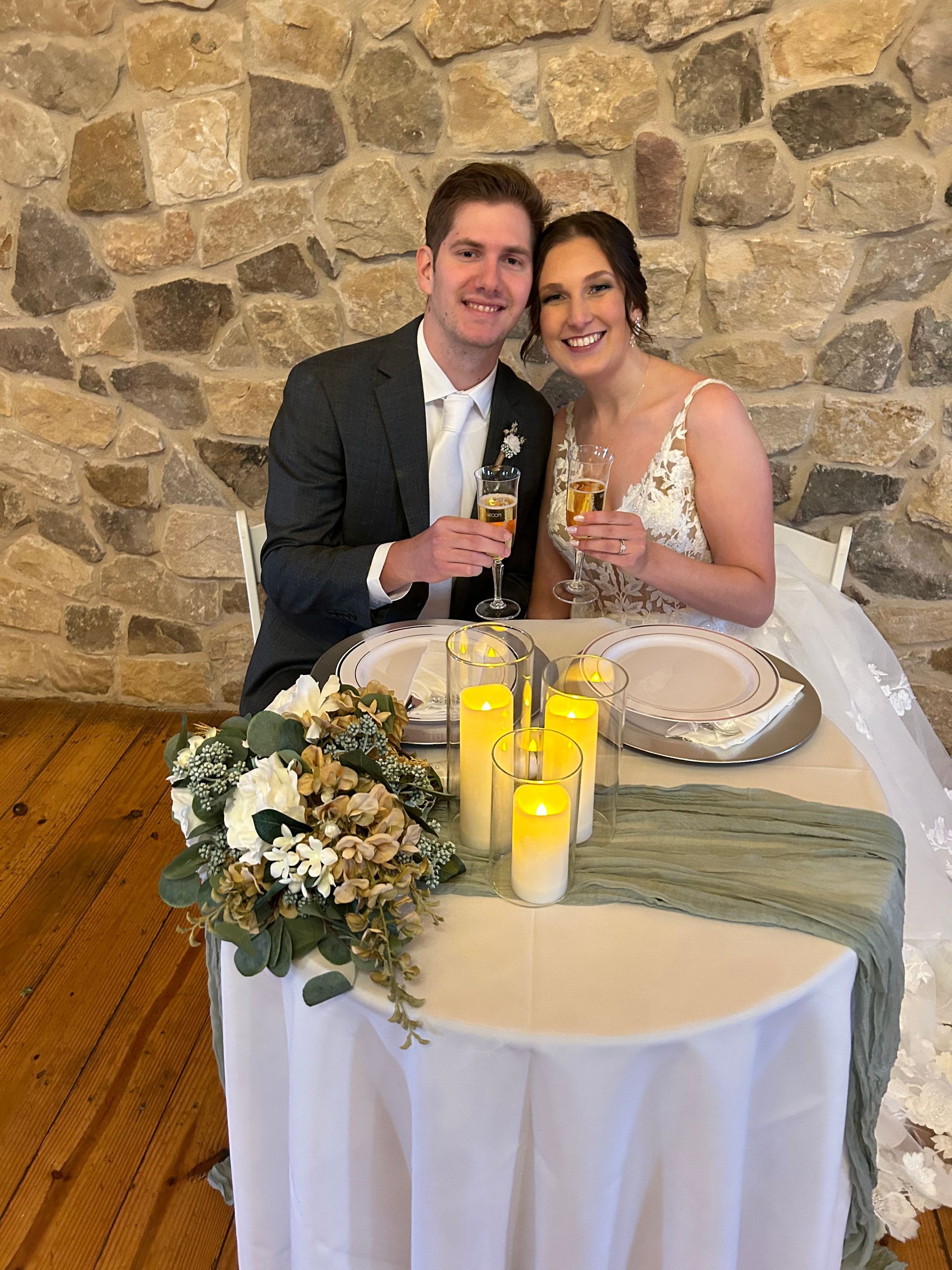 A bride and groom are sitting at a table holding champagne glasses.