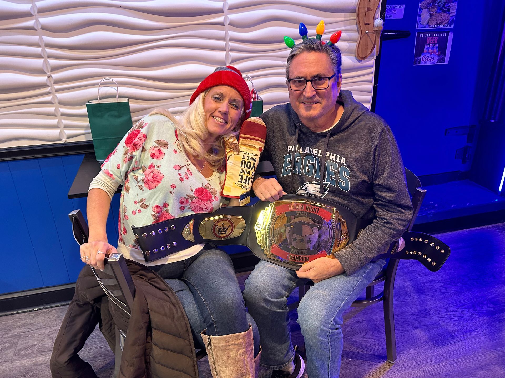 A man and a woman are sitting next to each other holding a wrestling belt.