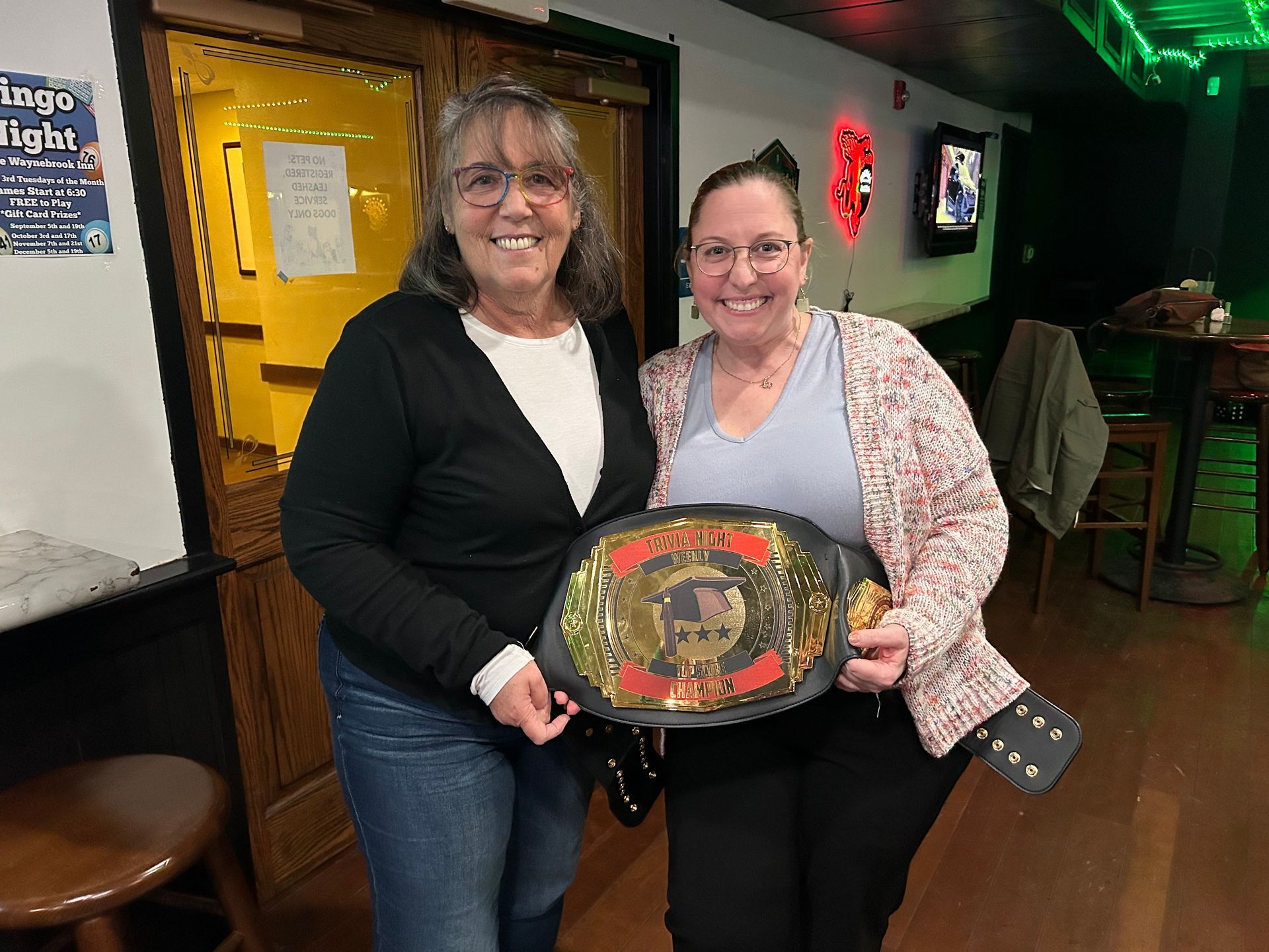 Two women are standing next to each other holding a wrestling belt.