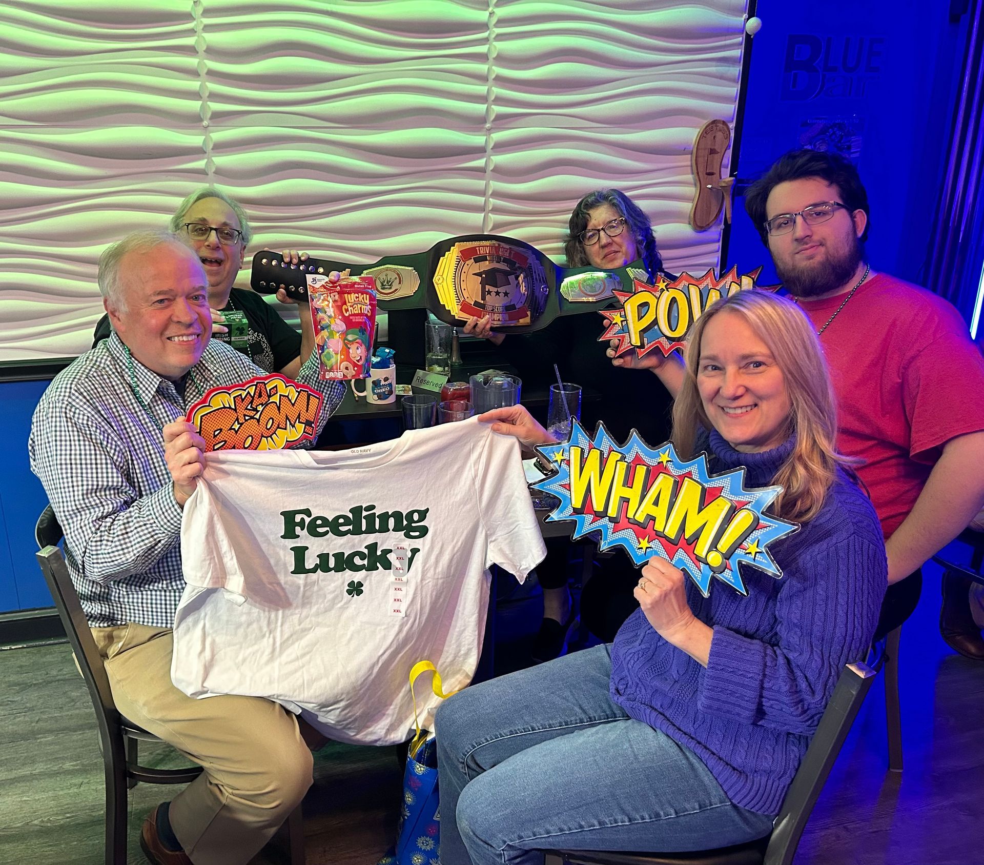 A group of people are sitting at a table holding a t-shirt that says feeling lucky.