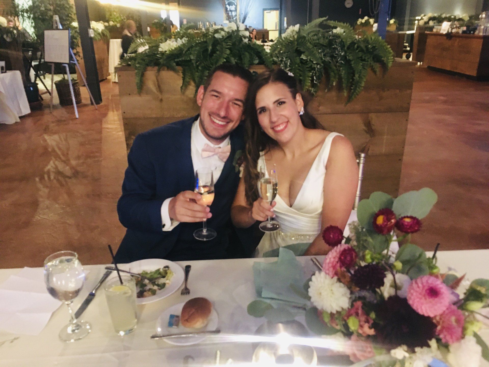 A bride and groom are sitting at a table holding champagne glasses.