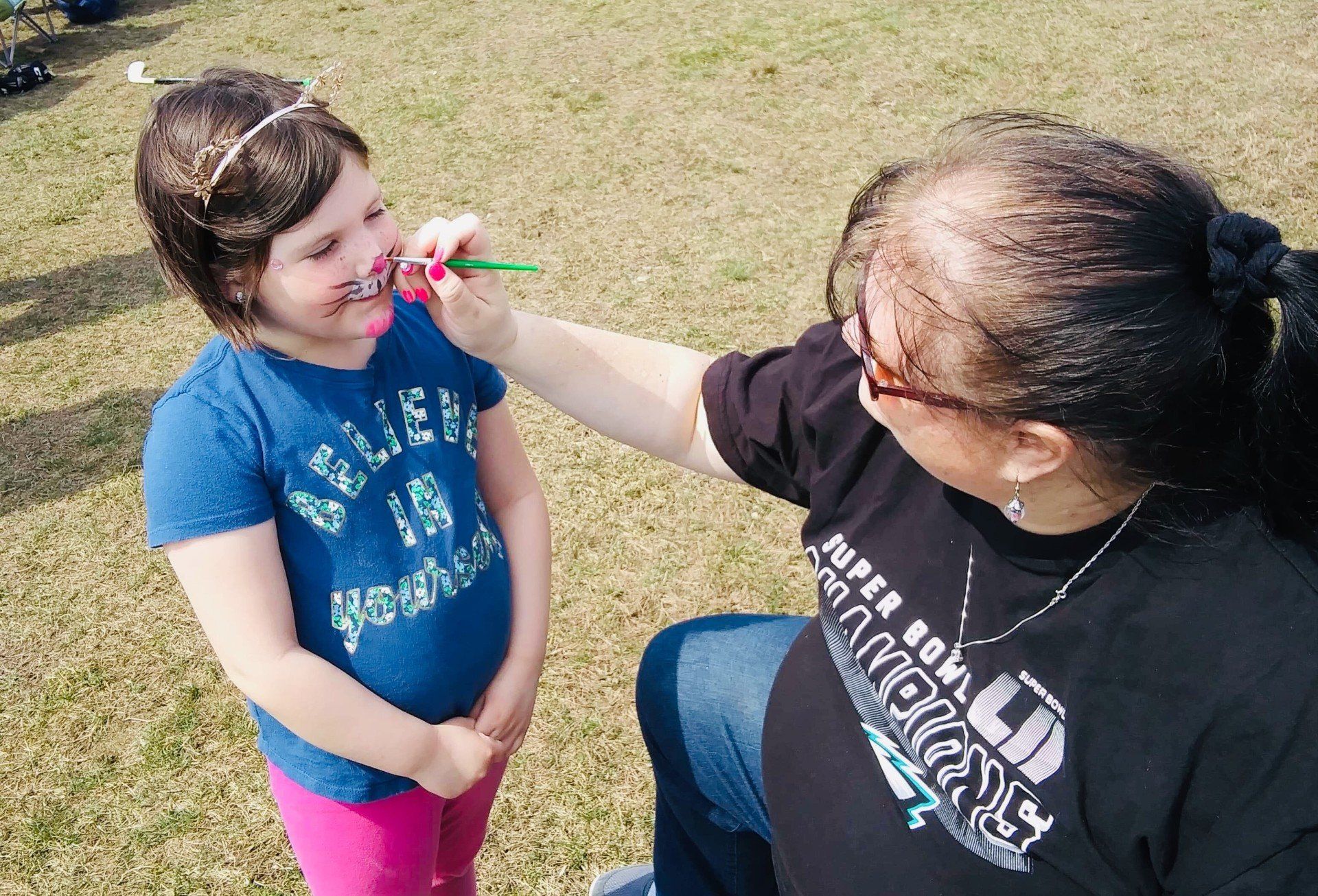 A woman is painting a little girl 's face with a brush.