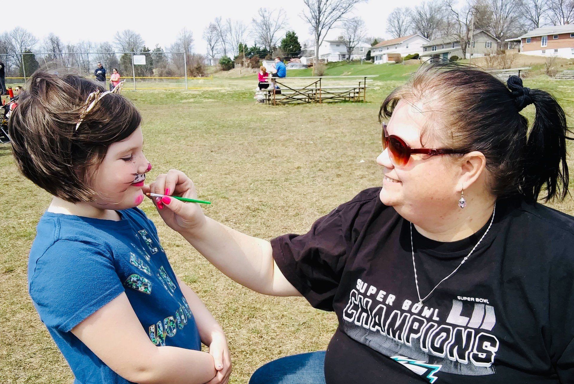 A woman in a super bowl champions shirt is putting lipstick on a little girl 's face