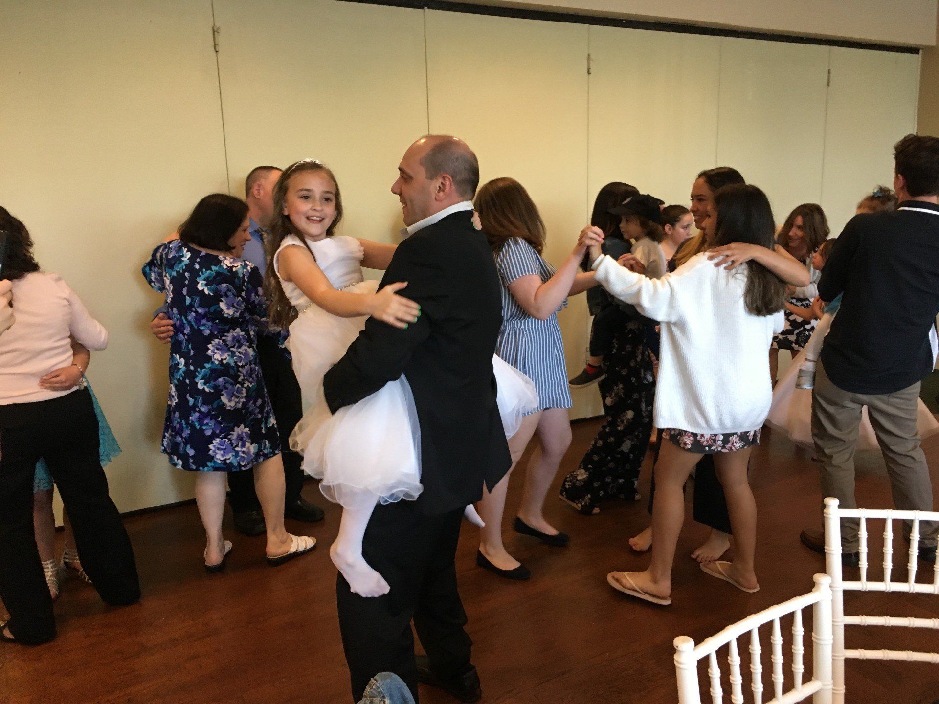 A man is holding a little girl in his arms while dancing with other people.