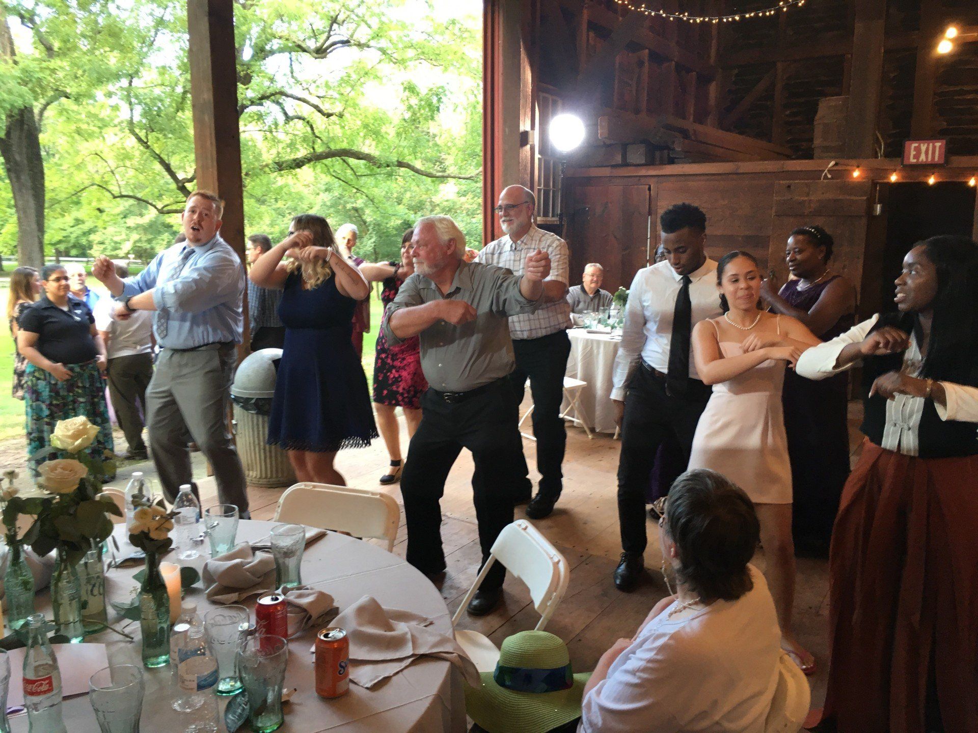A group of people are dancing at a wedding reception in a barn.