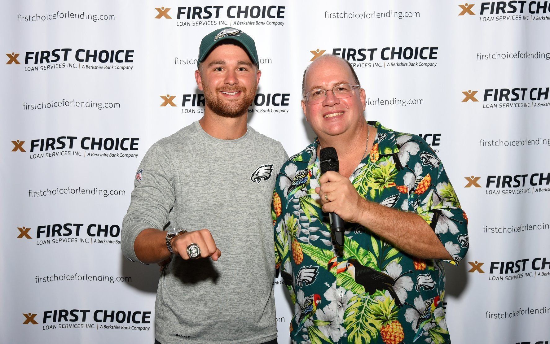 Two men are standing next to each other in front of a wall that says first choice.