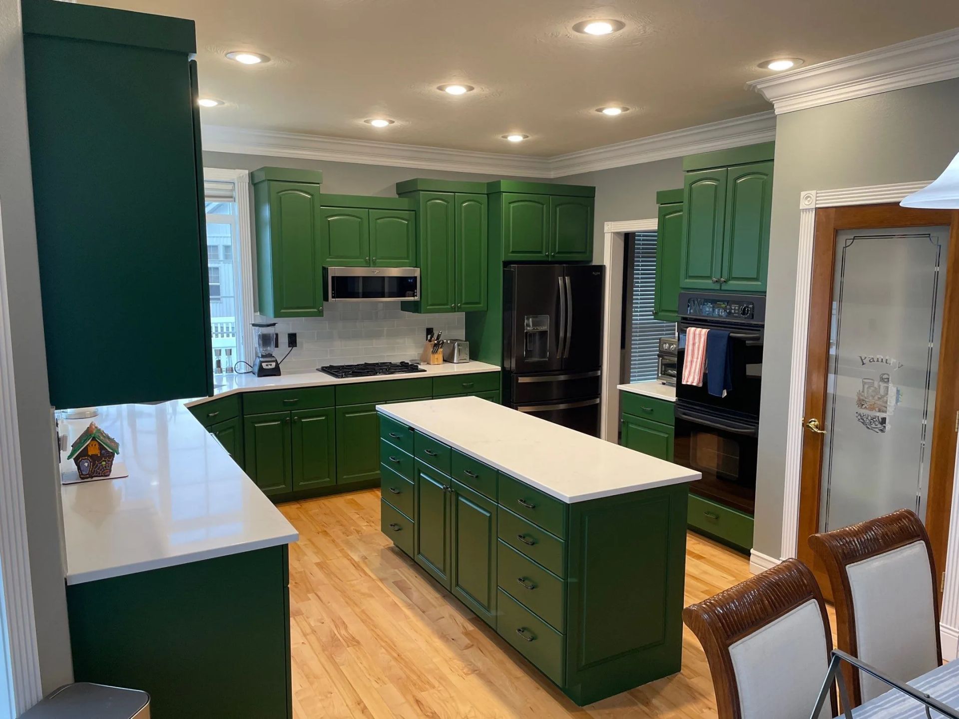 Bright green kitchen with a white island, black appliances, and wood floors