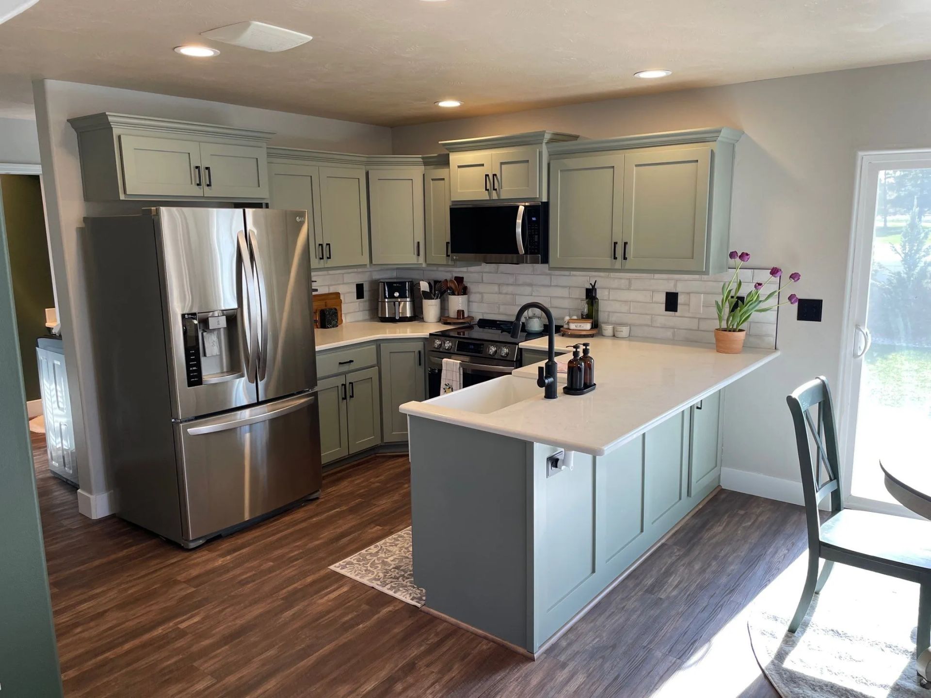 Modern kitchen with stainless steel refrigerator, white cabinets, island, and hardwood floors