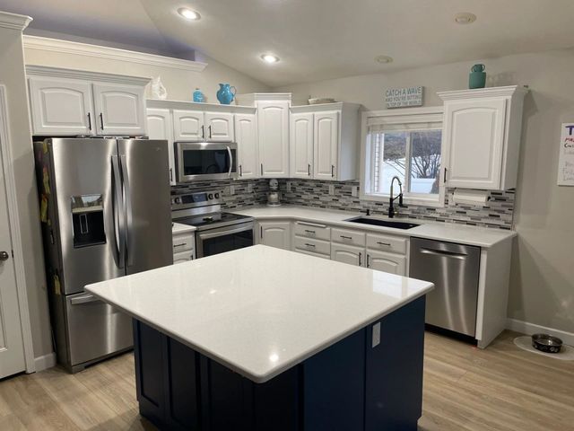 Bright modern kitchen with white cabinets, stainless steel appliances, and a navy island.