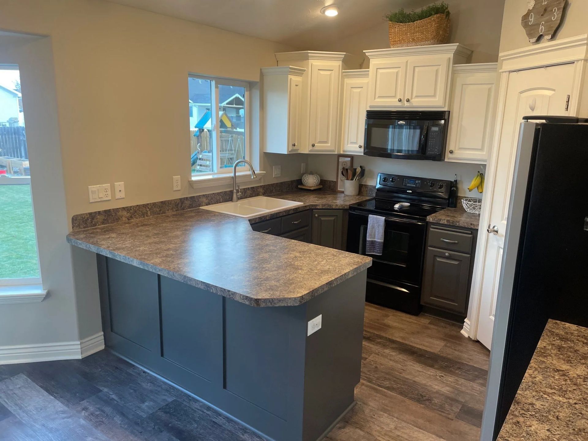 Modern kitchen with gray island, white cabinets, black appliances, and wood-look flooring