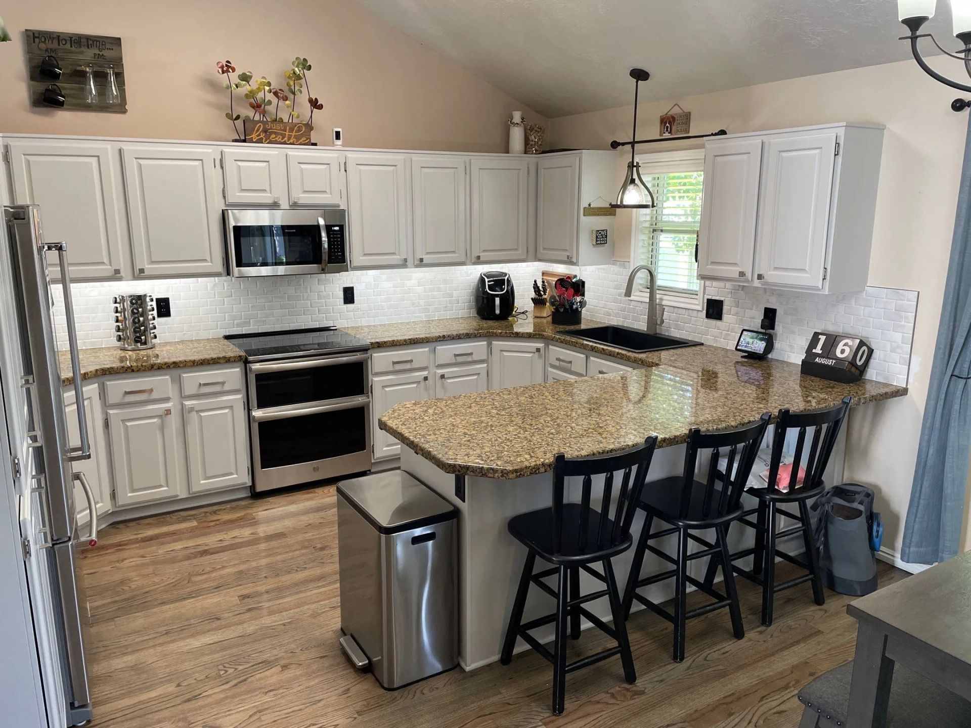 Bright kitchen with white cabinets, granite island, stainless appliances, and three black stools.