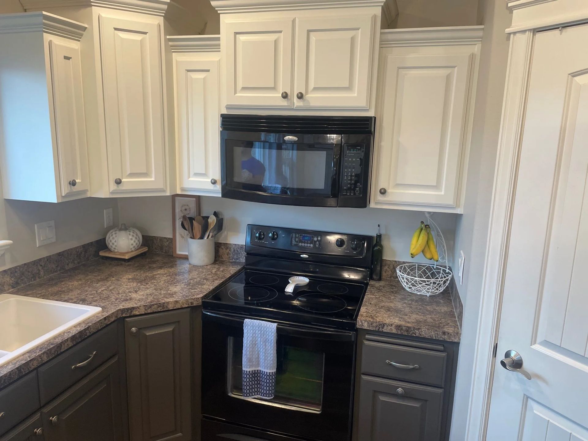 Compact kitchen with white cabinets, dark granite counters, black stove and microwave, and a dishwasher under the counter