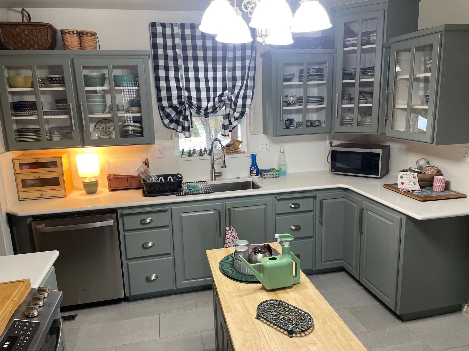 Gray kitchen with green cabinets, checkered curtain, hanging lights, and a small island with a green mixer