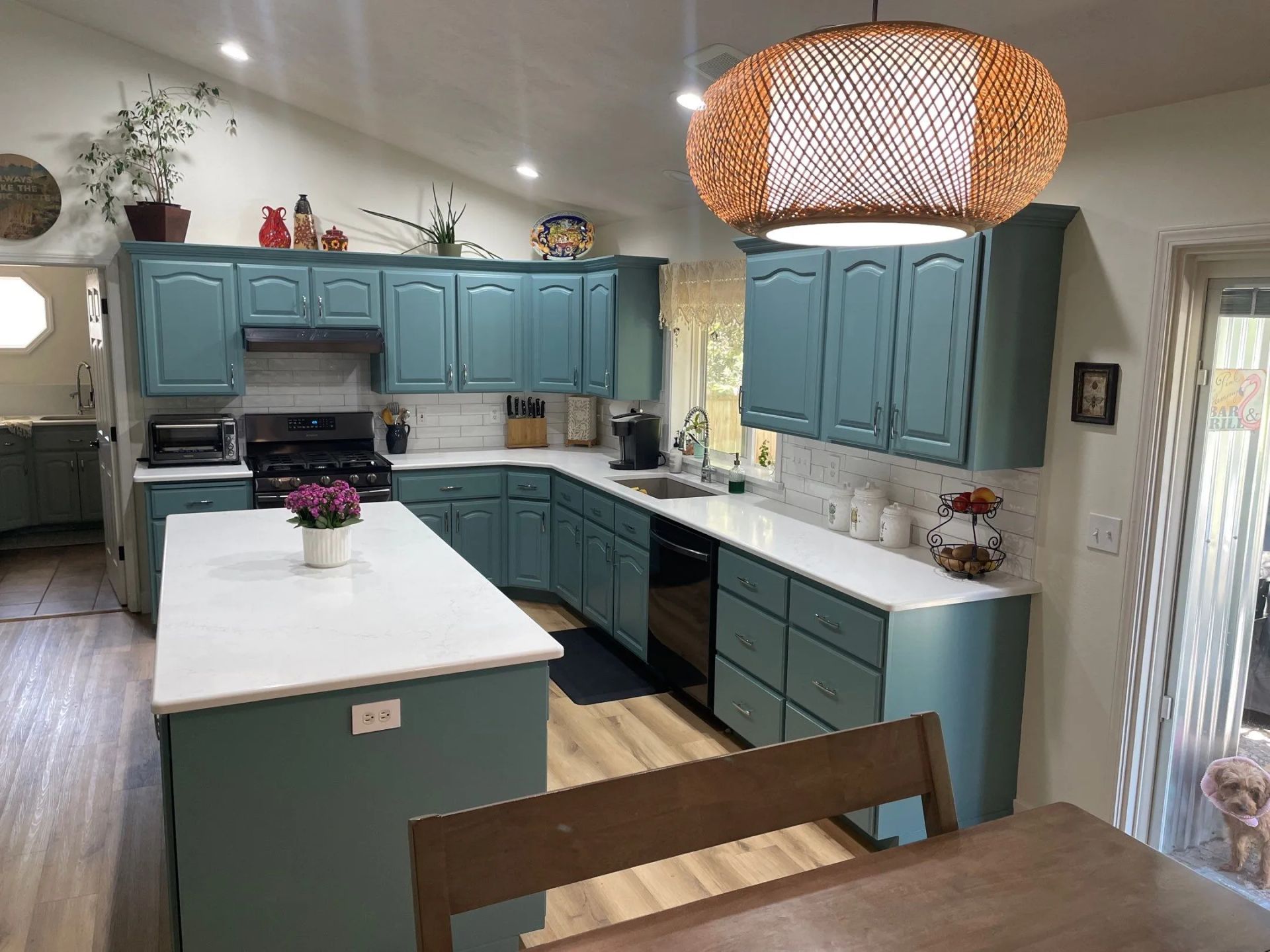 Teal kitchen with white island, dark countertops, and woven pendant light