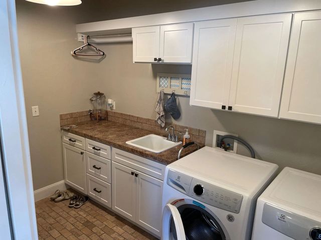 Laundry room with white cabinets, granite counter, sink, and stacked washer-dryer under wall cabinets