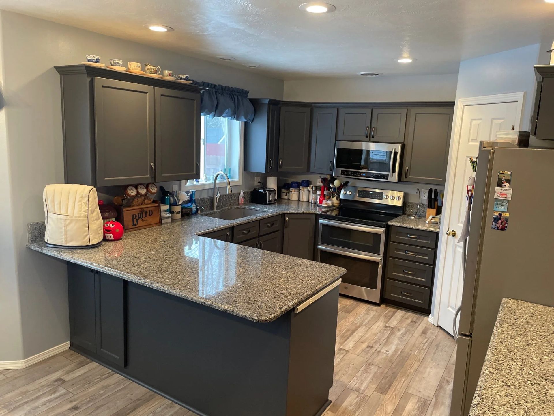 Modern kitchen with dark cabinets, granite island, stainless appliances, and light wood floor