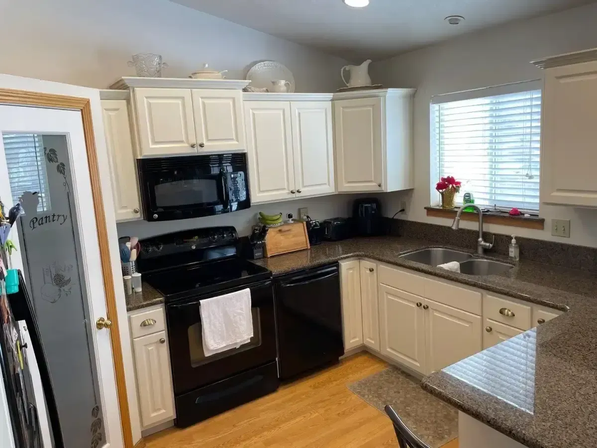 Bright kitchen with white cabinets, black appliances, granite counters, and a window over the sink.