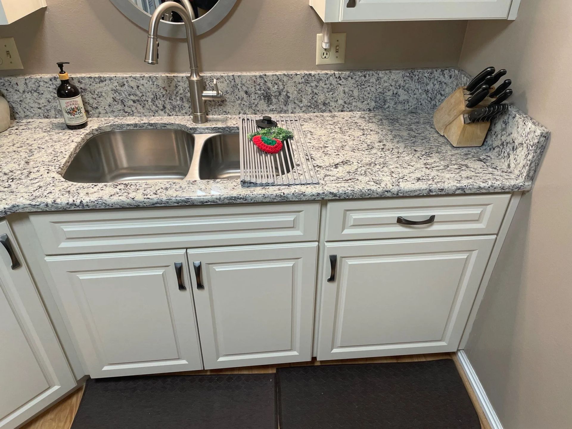 White bathroom vanity with granite countertop, sink, mirror, and decorative soap dispenser.