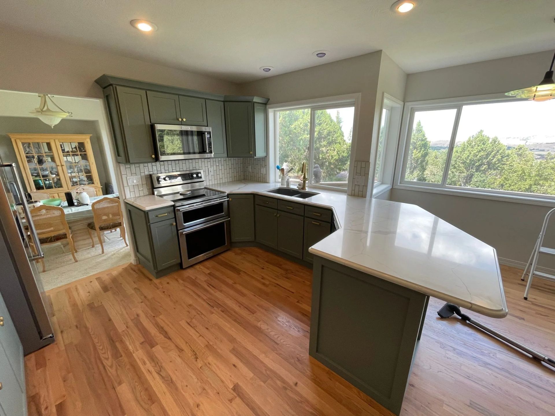 Bright kitchen with gray cabinets, wood floors, and a white island beside large windows