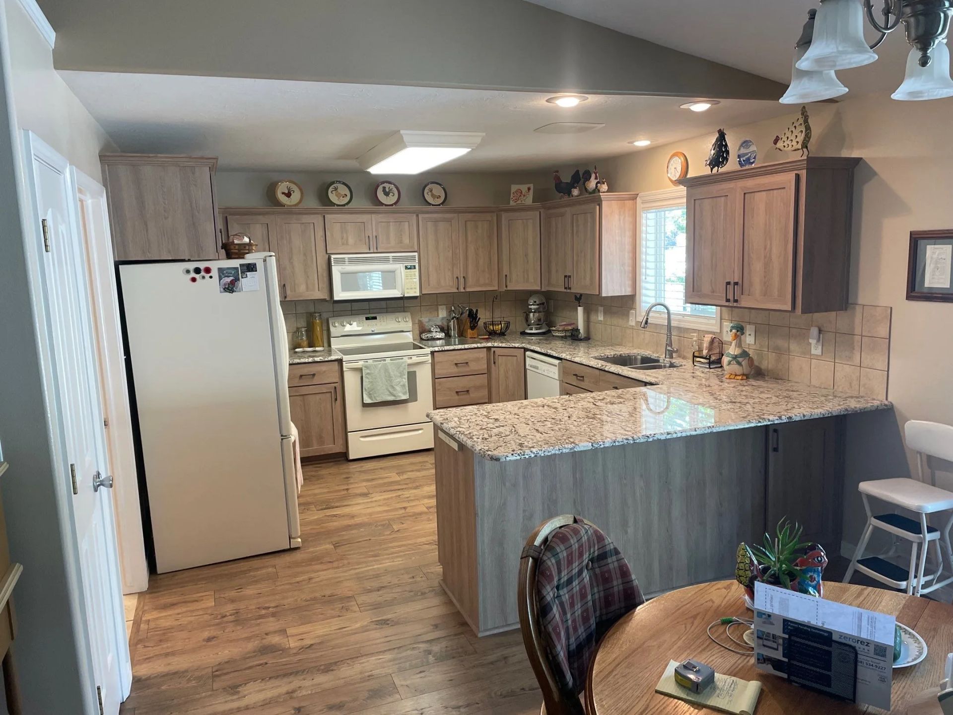 Kitchen with wood cabinets, white appliances, and a granite island in an open dining area.