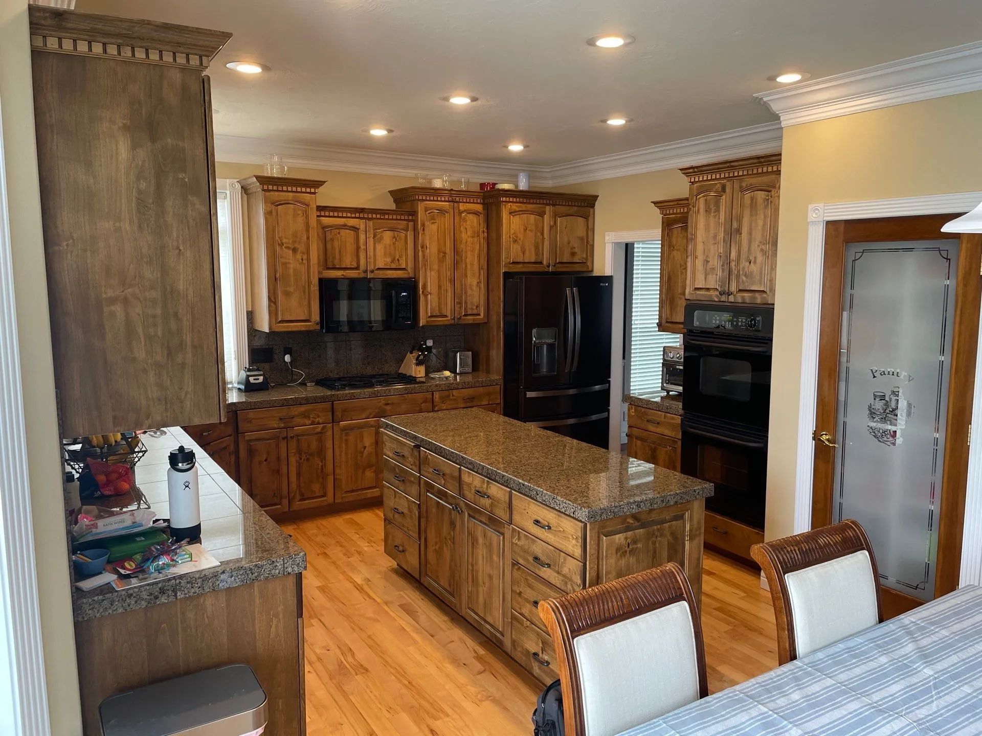 Spacious kitchen with wood cabinets, black appliances, island, and dining chairs in the foreground