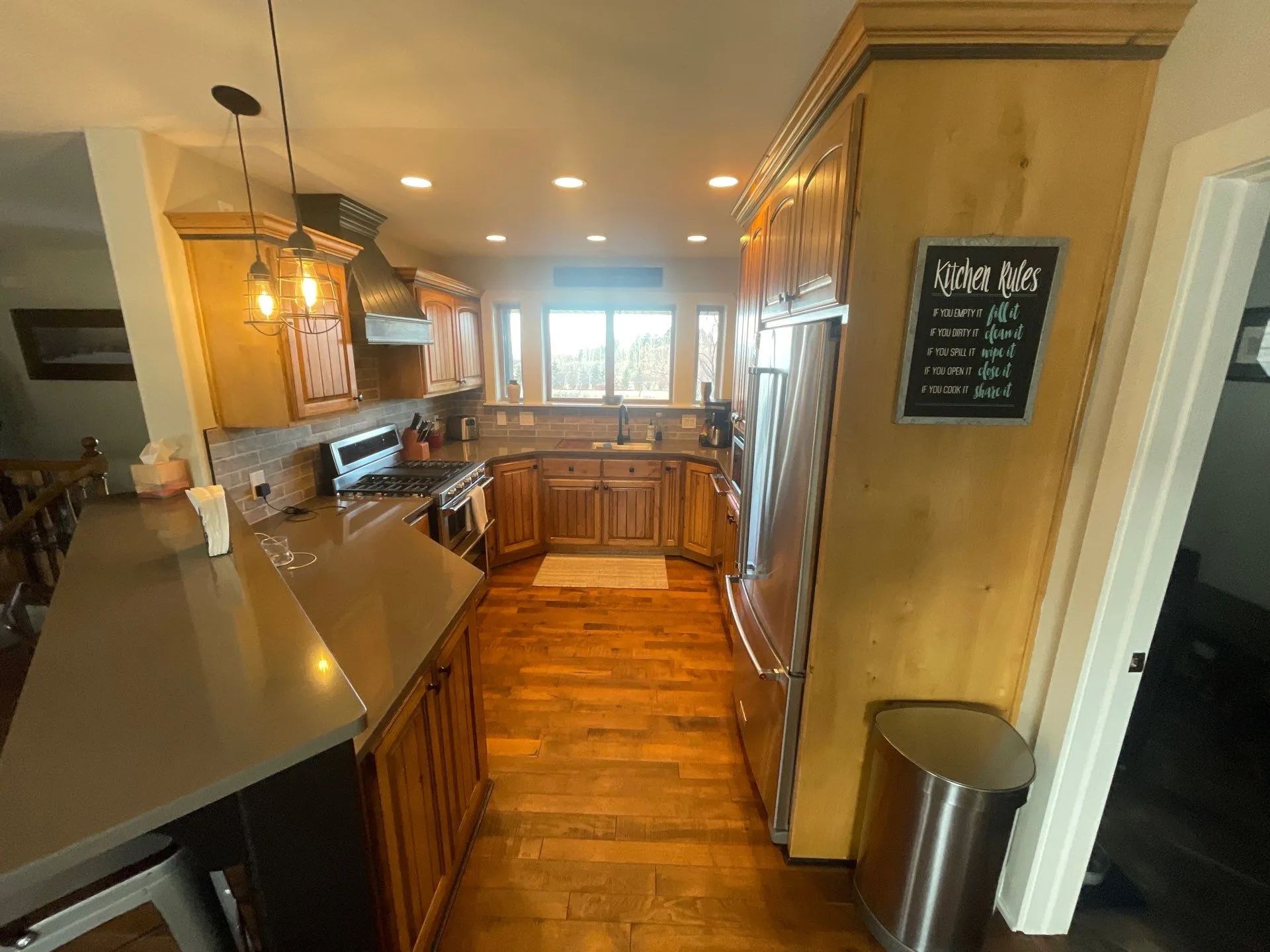 Narrow kitchen with wood cabinets, stainless appliances, and a wooden floor, viewed toward a bright back doorway