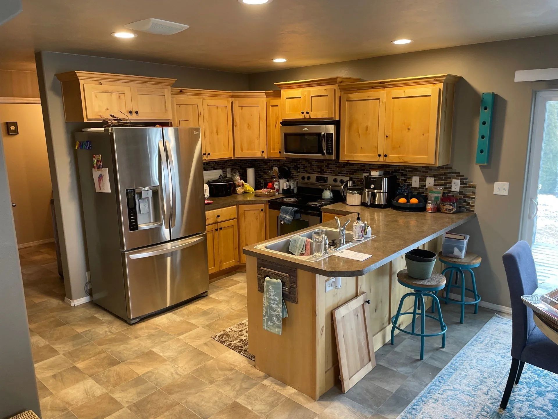 Kitchen with stainless steel appliances, wood cabinets, and a tiled island with two stools in warm lighting