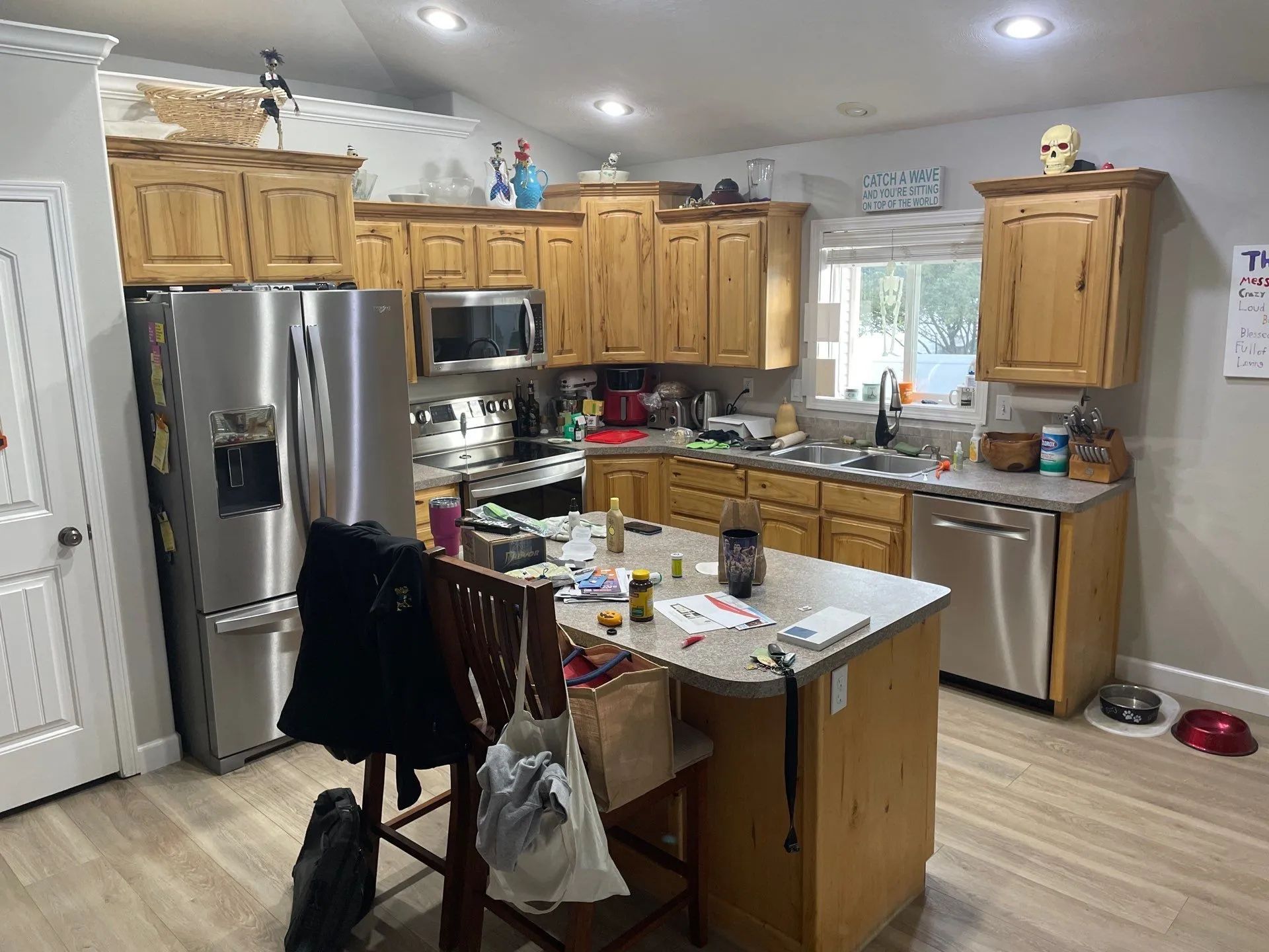 Kitchen with wooden cabinets, stainless steel appliances, island cluttered with items, and a window over the sink.