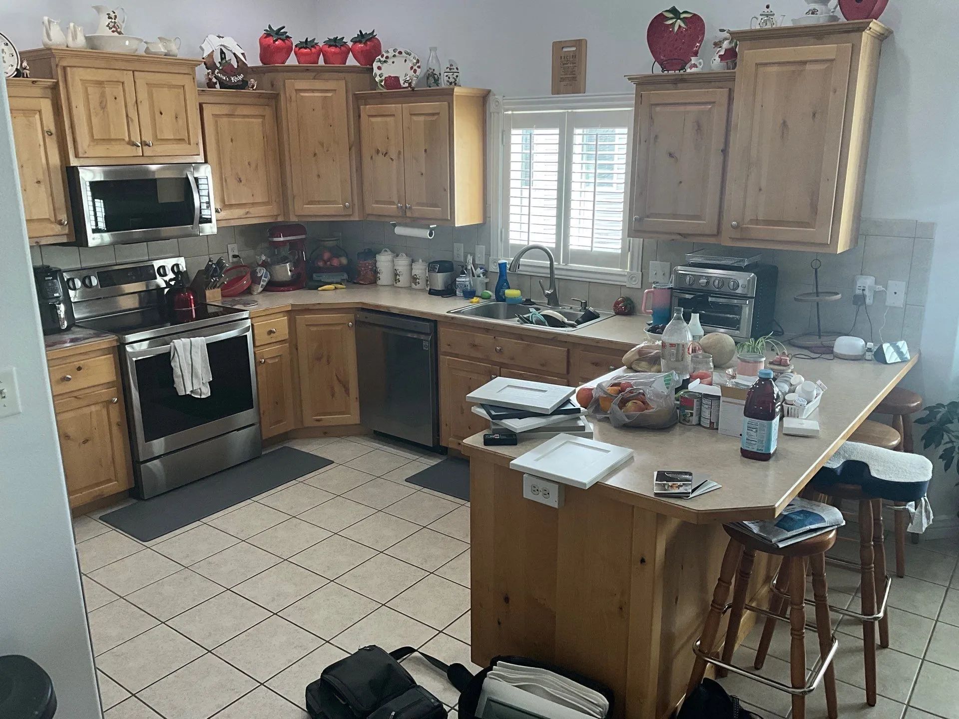 Kitchen with wooden cabinets, tiled floor, stove, island, and window above the sink, cluttered with items.