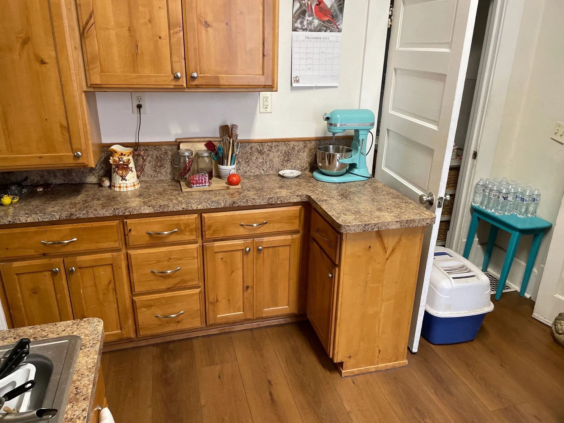 Wooden kitchen with granite counters, coffee maker, open door, and pet gate near a blue stool