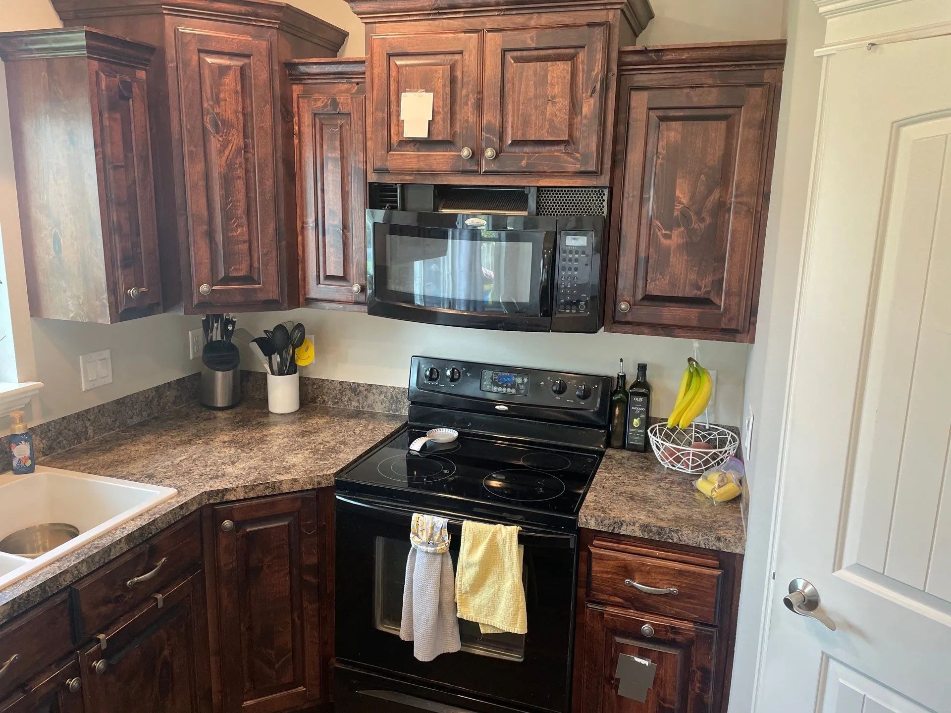 Kitchen with dark wood cabinets, black stove and microwave, granite counters, and bananas on the counter.