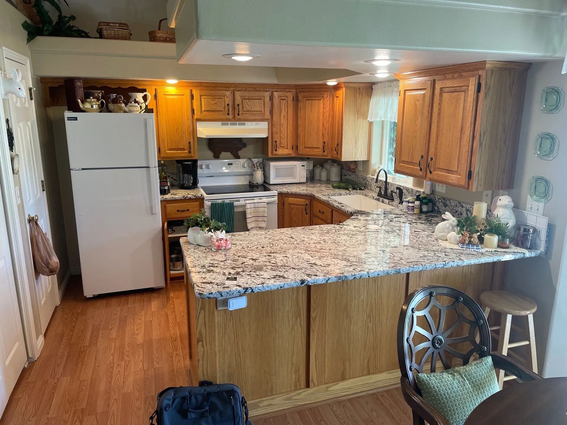 Kitchen with white appliances, wood cabinets, and a large granite island under warm lighting