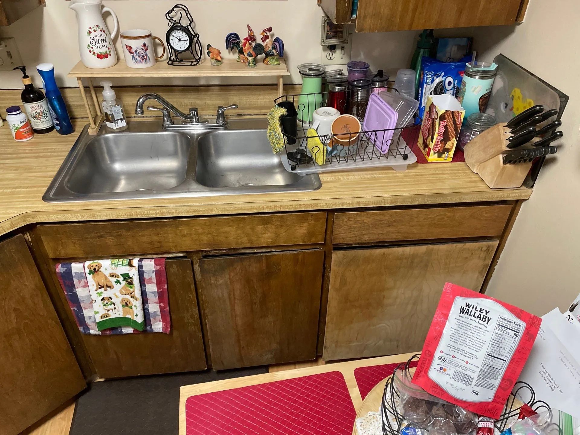 Kitchen sink and counter with dishes, bottles, decor, and red package on a tiled floor.