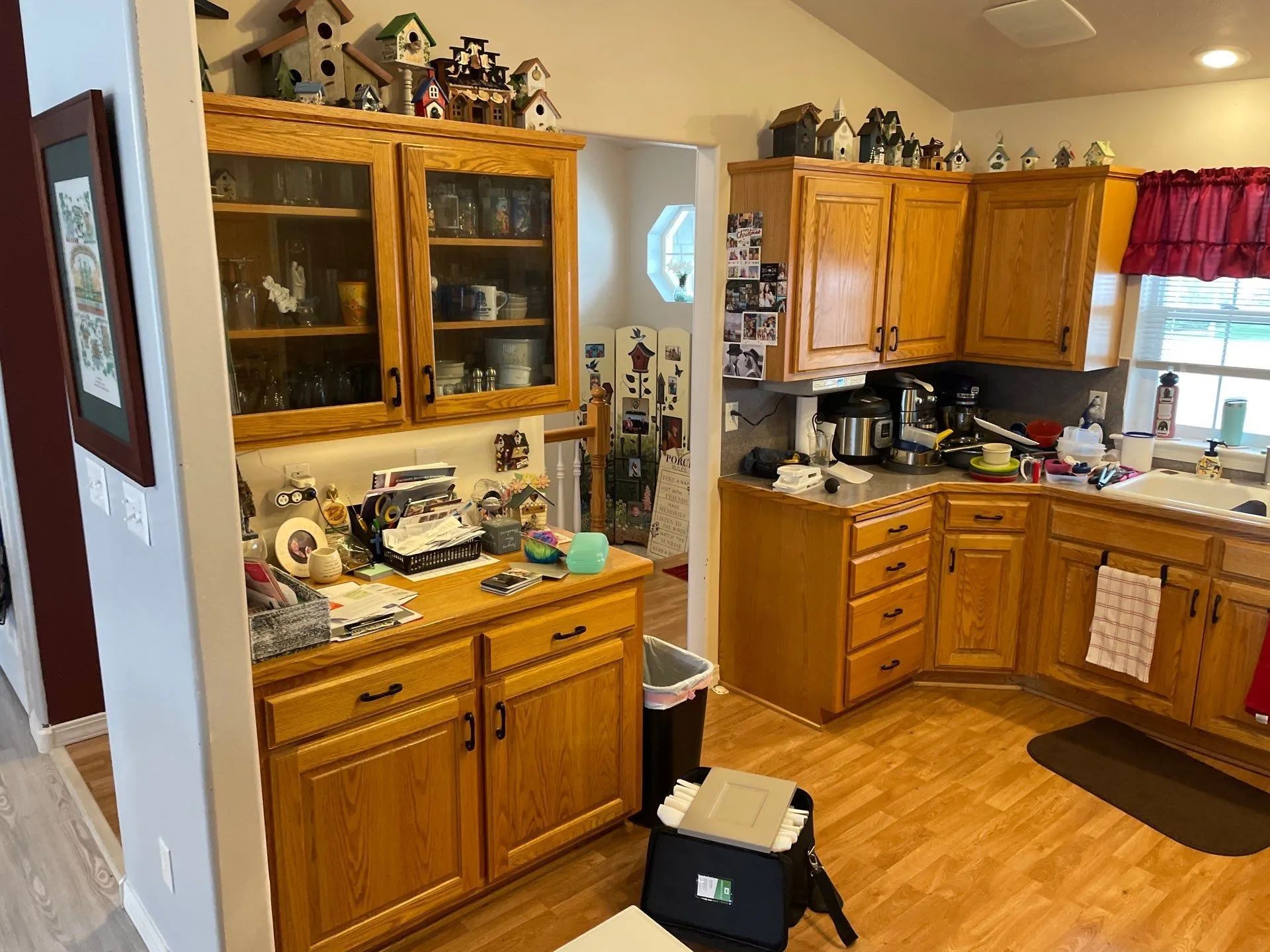 Wooden kitchen with cabinets, a counter full of items, and warm hardwood floors.