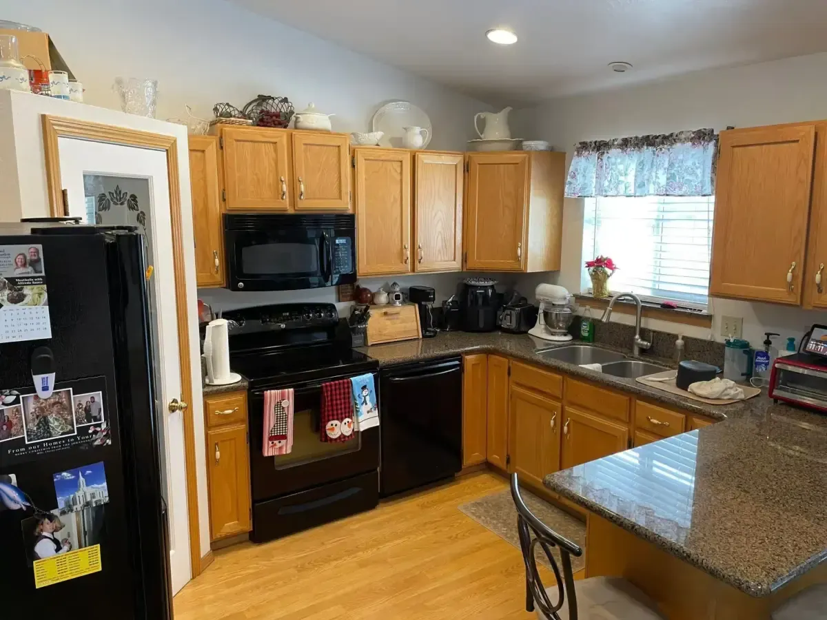 Kitchen with wooden cabinets, black appliances, granite counters, and a window over the sink.