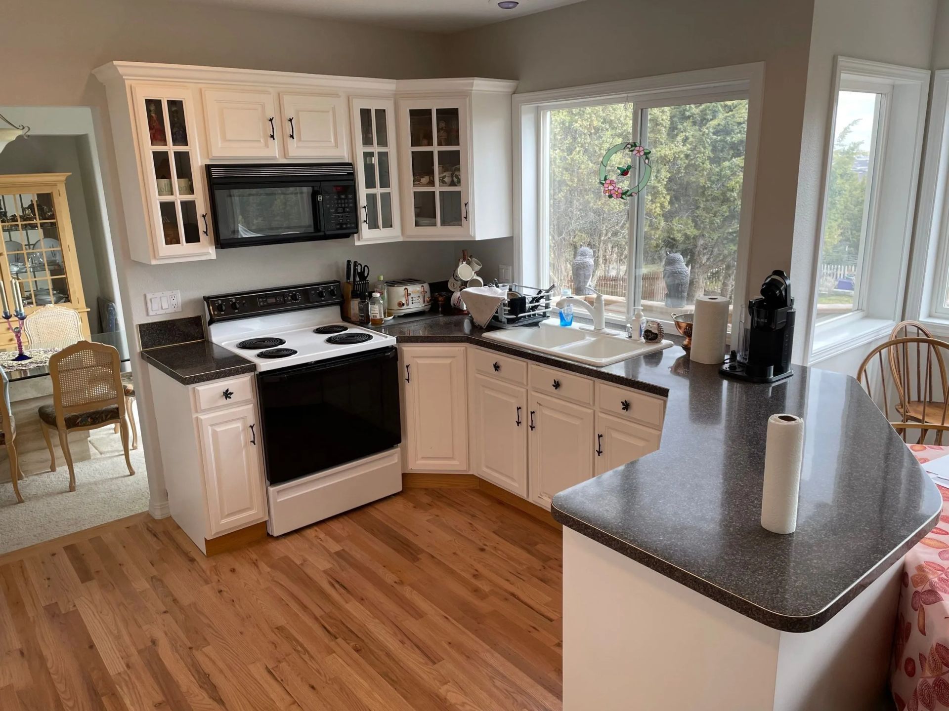 Bright kitchen with white cabinets, black stove, gray countertops, and a large window.