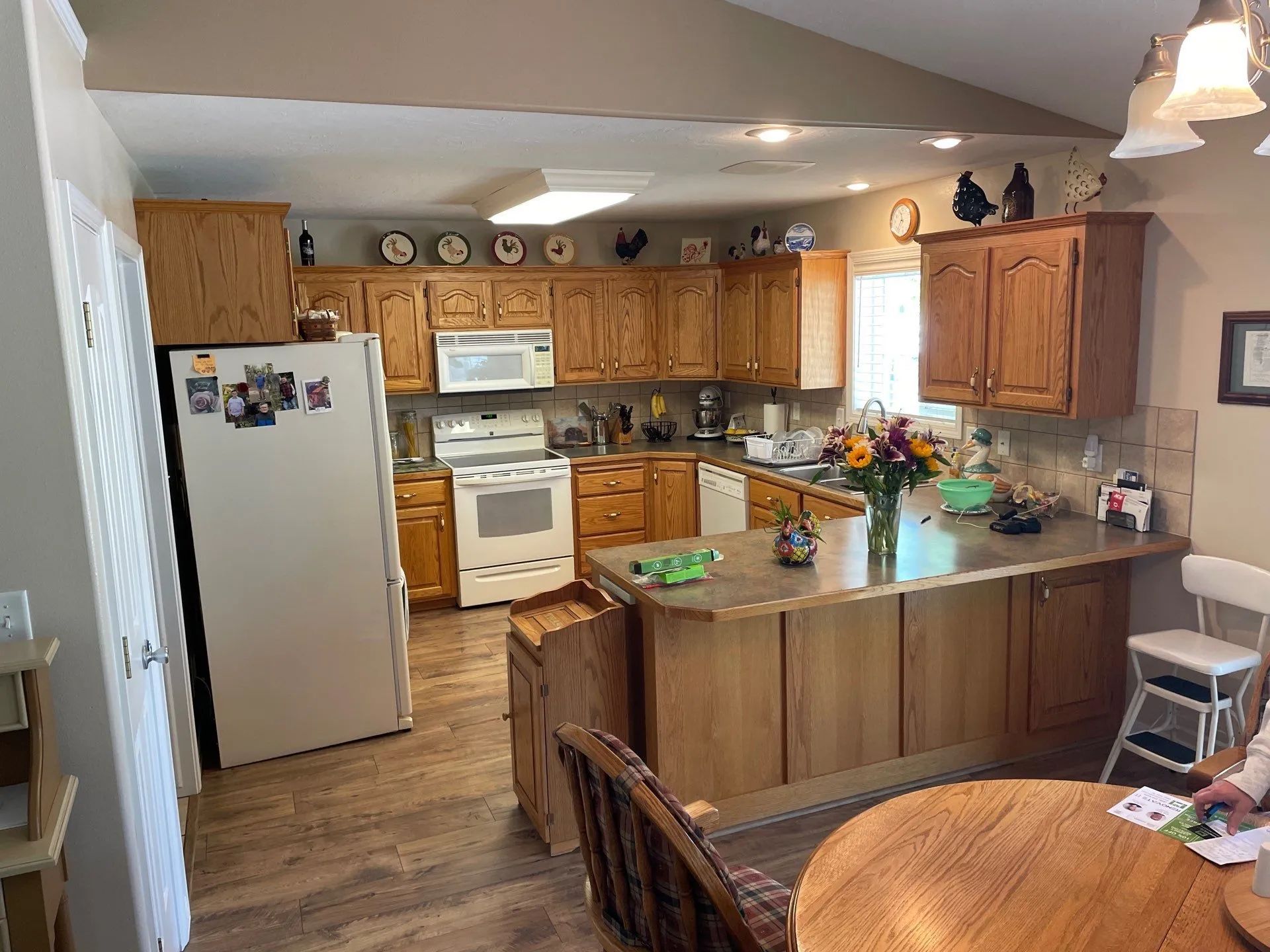 Small kitchen with wood cabinets, white appliances, island, and a round table in the foreground.