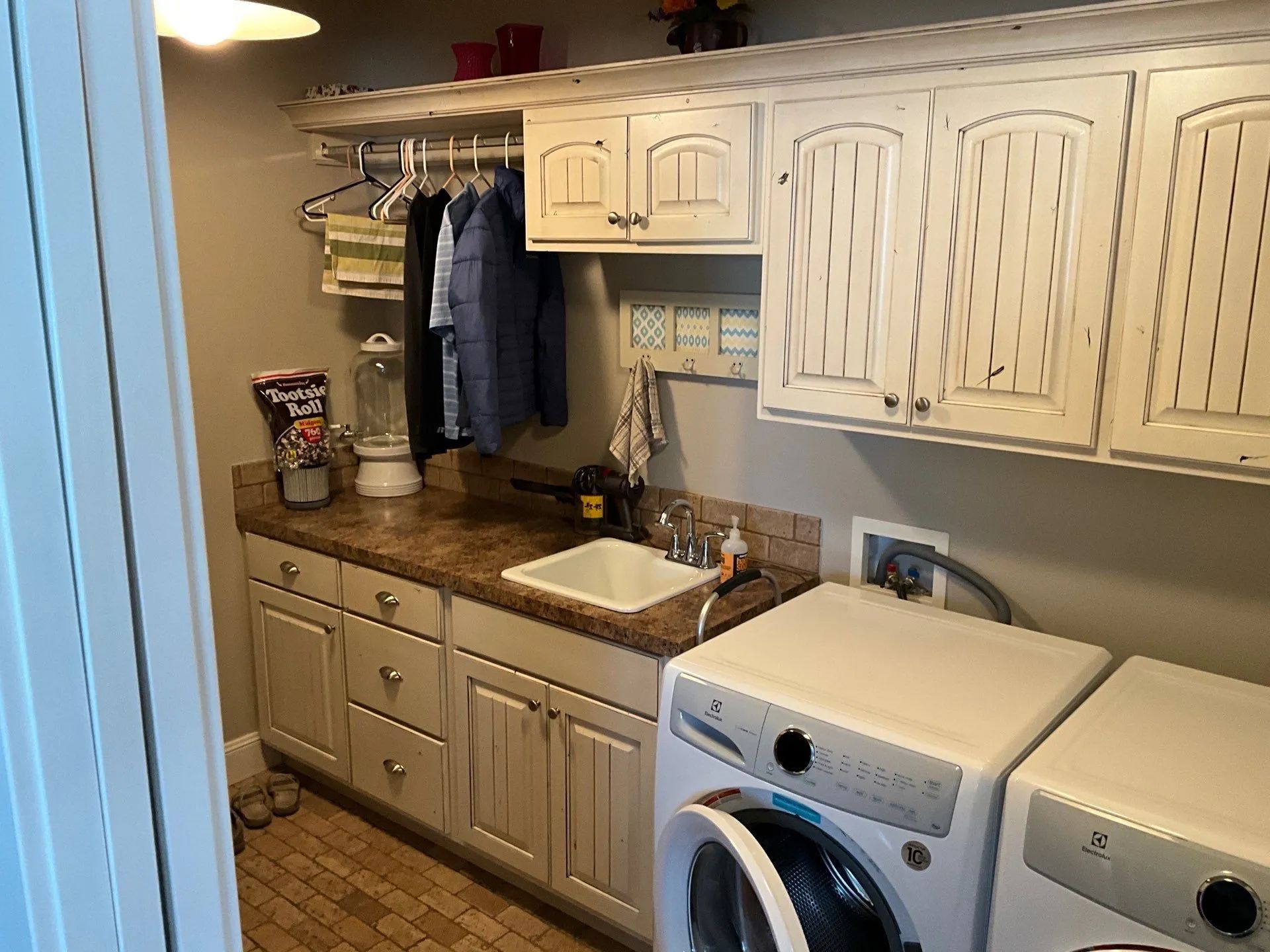 Laundry room with white cabinets, wood countertop, sink, and washer and dryer beside hanging clothes.