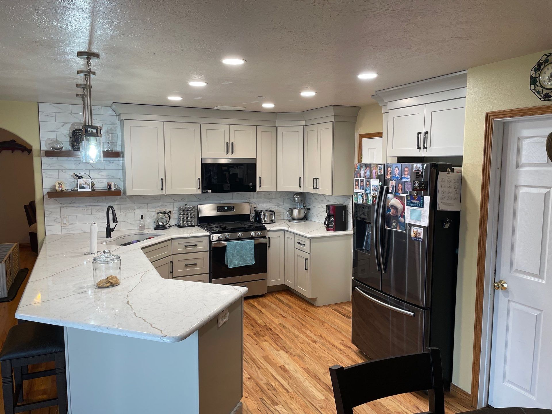 Modern kitchen with white cabinets, stainless appliances, wood floors, and a black refrigerator.