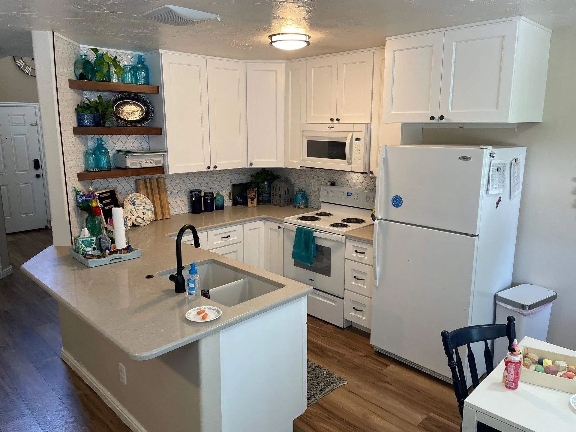 Bright kitchen with white cabinets, gray countertops, a white fridge, and a small dining table.