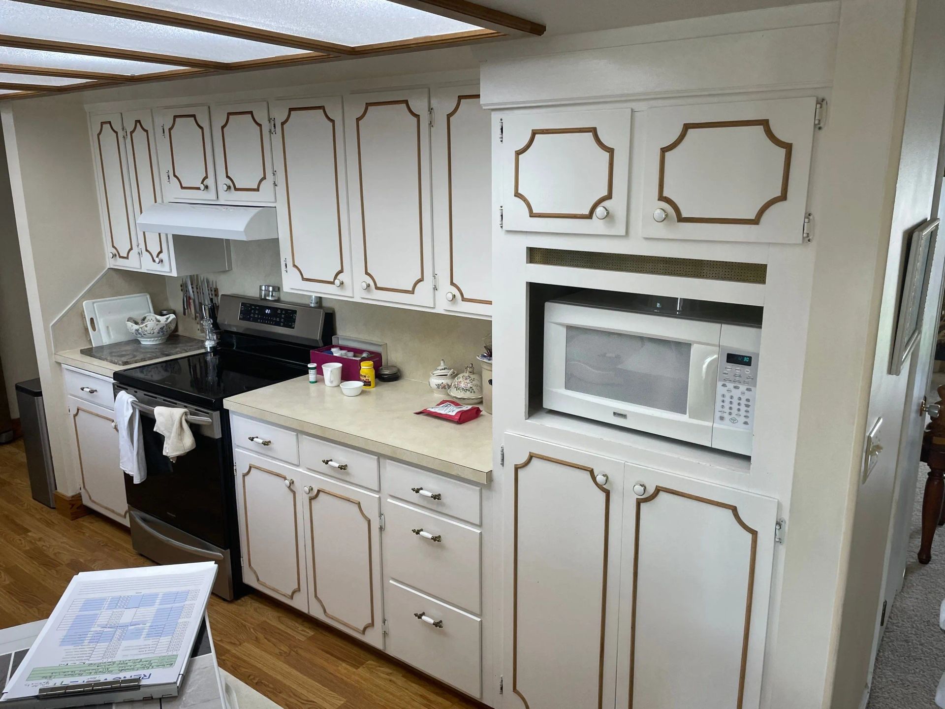 Small white kitchen with cabinets, stove, microwave, and countertop under bright skylight.