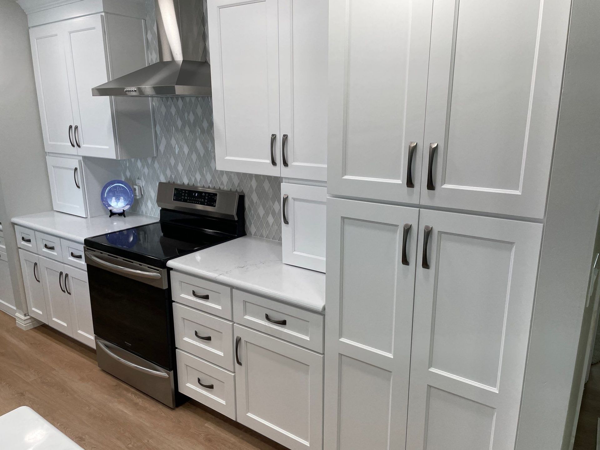 Modern white kitchen with stainless-steel stove, range hood, cabinets, and wood floor