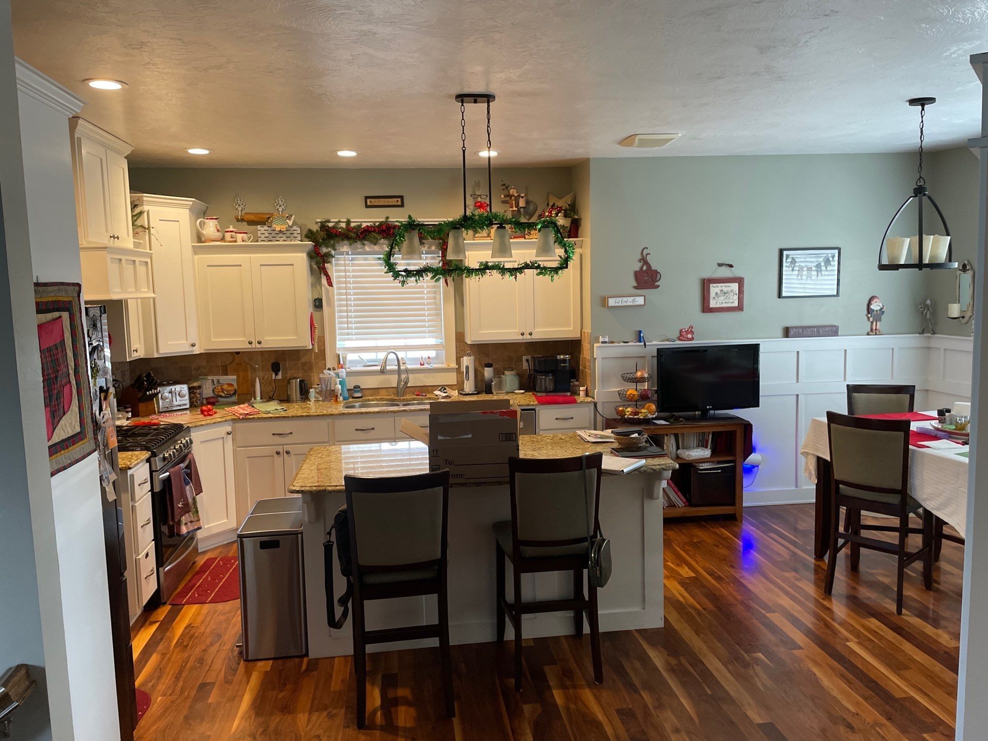 Open-plan kitchen and dining area with island, chairs, wood floors, and holiday garland over the window.