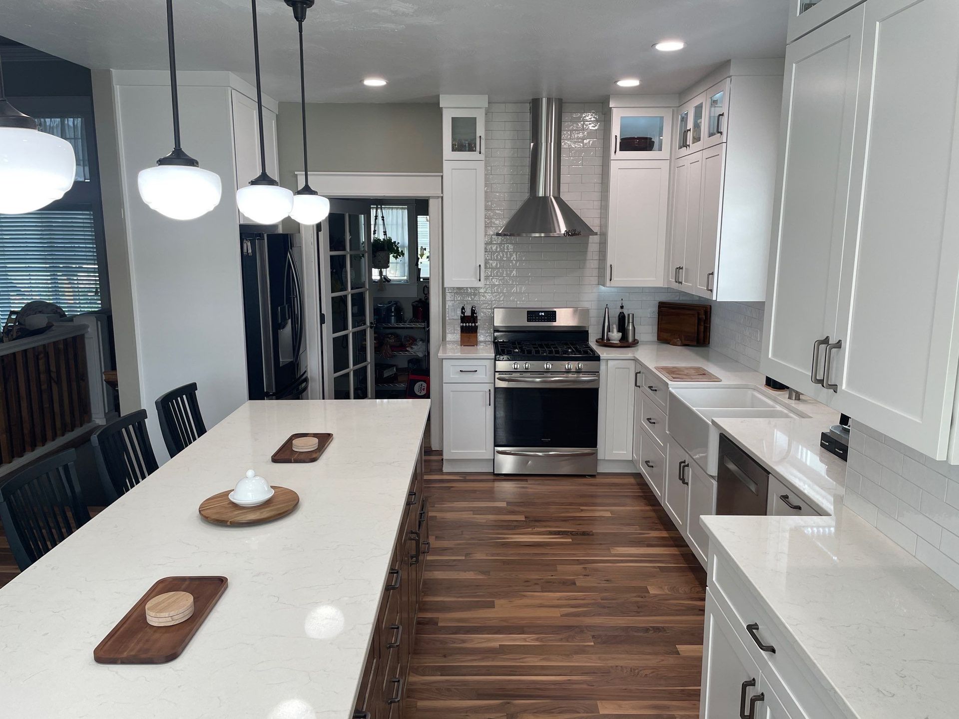 Modern white kitchen with long island, pendant lights, stainless steel appliances, and wood floors